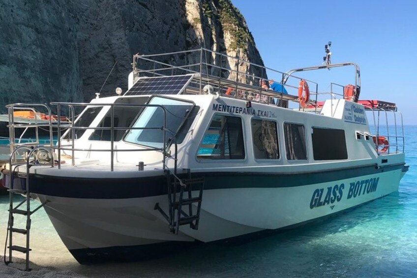 A boat named 'GLASS BOTTOM' docked at a rocky coastal area with clear blue water. 1