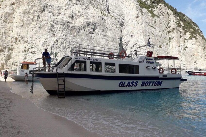 A boat named 'GLASS BOTTOM' docked at a beach with rocky cliffs in the background. 2