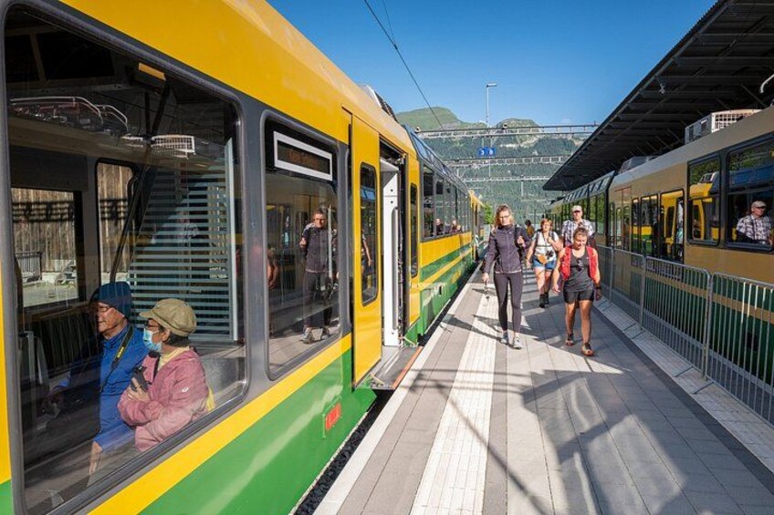 Un quai de gare où des passagers montent et descendent d’un train jaune et vert. 4