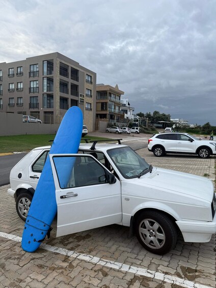 A white car with a blue surfboard mounted on the roof. 3