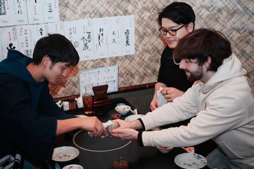 Tres personas jugando un juego de mesa en un restaurante con menús japoneses y una decoración tradicional. 3
