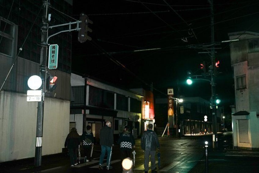 Una escena nocturna en la calle con peatones, semáforos y letreros iluminados. 2