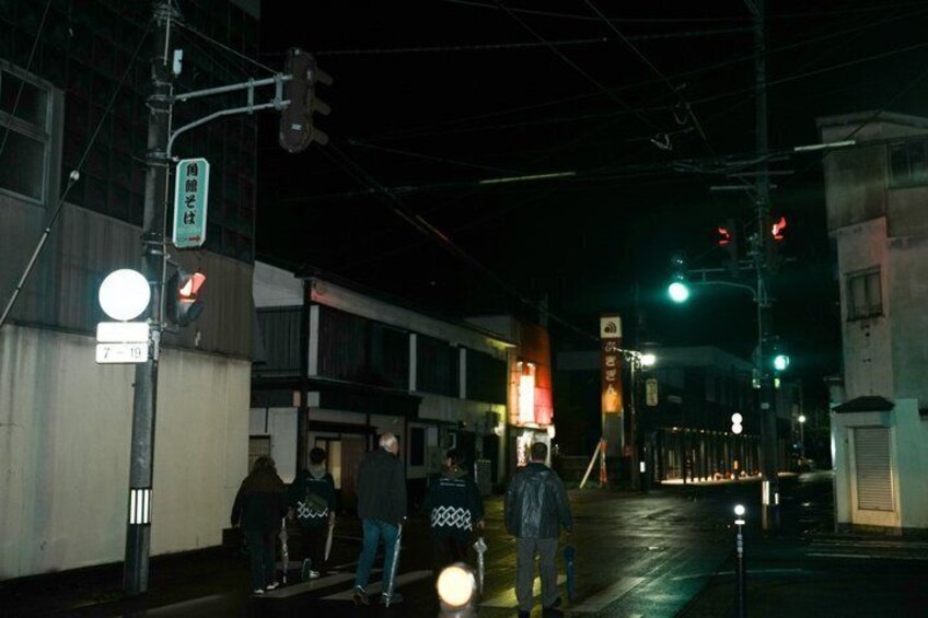 A nighttime street scene with pedestrians, traffic lights, and illuminated signs. 2