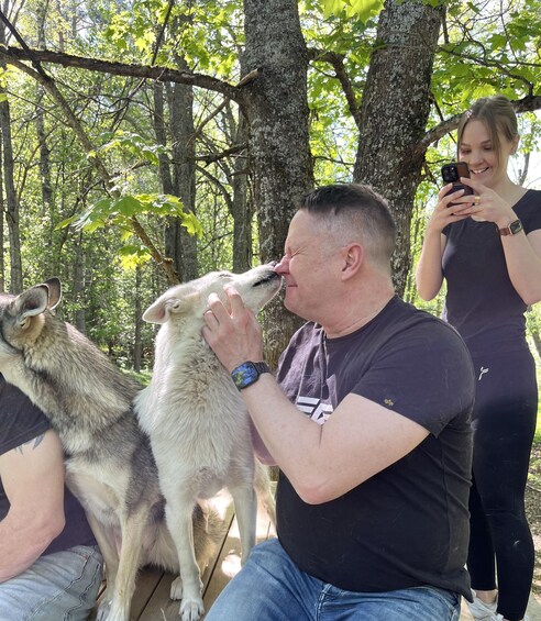 A man kissing a dog, surrounded by trees in a wooded area. 4