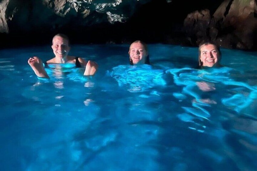 Three people in a blue-lit swimming pool with rocky formations in the background. 1