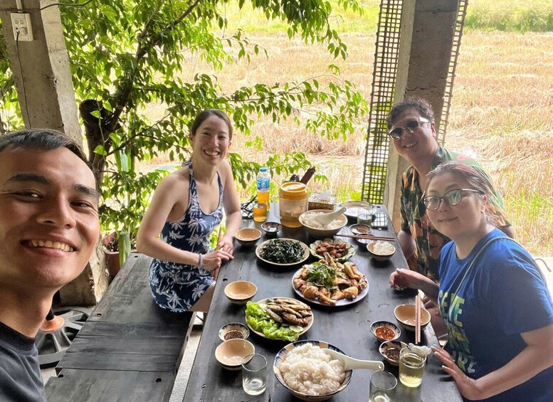 A group of people dining outdoors at a wooden table with various dishes and drinks. 5