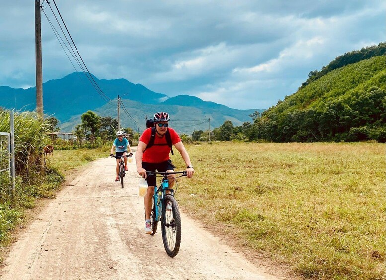 Two cyclists on a dirt road with mountains in the background. 3