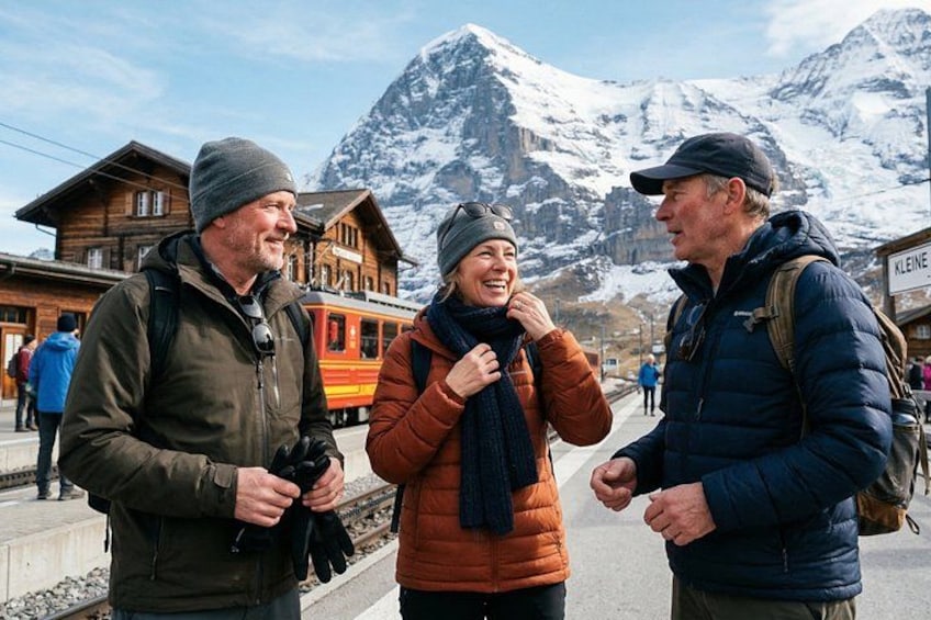 Three people standing by a train station with a mountain in the background. 1