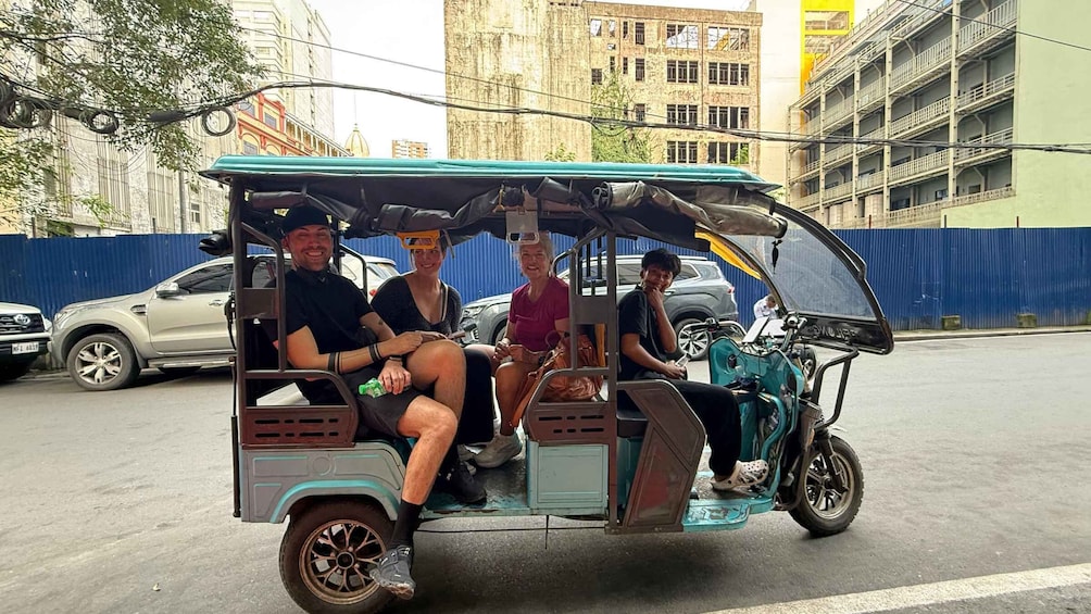 A tuk-tuk with three passengers on a city street. 2