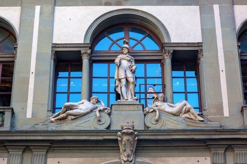 En klassisk bygningsfacade med en central statue, hvælvede vinduer og dekorative støbninger. 2