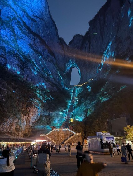 A night scene with a large rock formation featuring a natural archway, illuminated by blue lights. 4