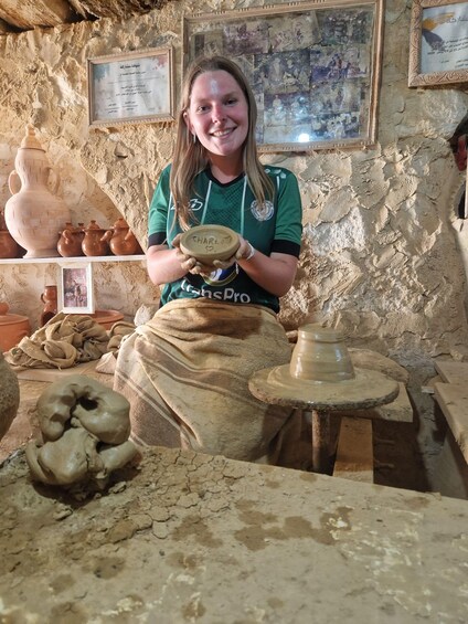 A person in a pottery workshop, surrounded by pottery wheels, clay pots, and tools. 5