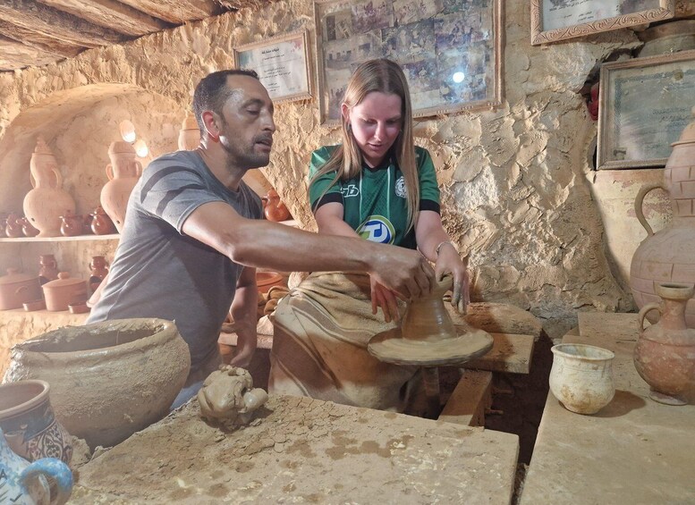 Two people engaged in pottery making, surrounded by various clay pots and pottery wheels. 1