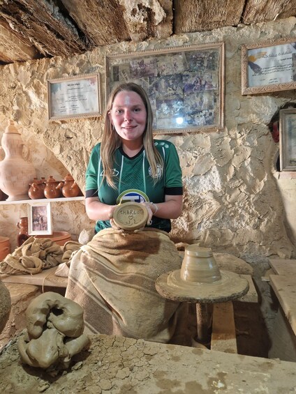 A person at a pottery workshop with clay pots and a wheel. 2