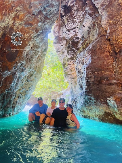 A group of people sitting in a natural pool with a waterfall in a rocky cave. 3