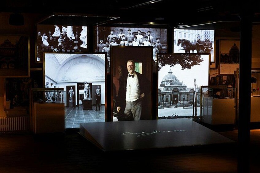A museum exhibit with a central portrait, surrounded by historical photographs and artifacts. 2