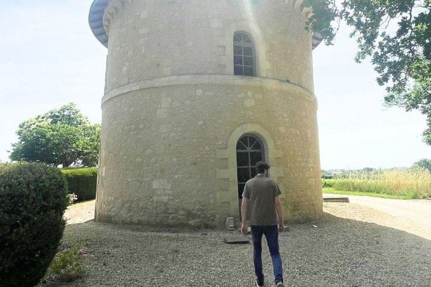 A stone tower with a rounded top and arched windows, surrounded by gravel and greenery. 4