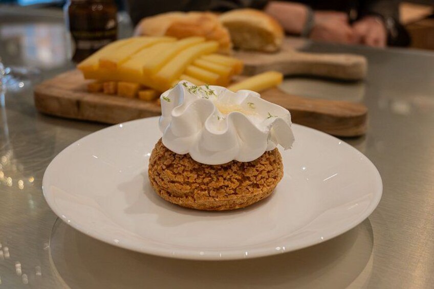 A dessert on a white plate with whipped cream on top, a wooden cutting board with cheese and fries in the background. 5