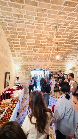 A group of people in a stone-walled room with a table of food and wine. 4