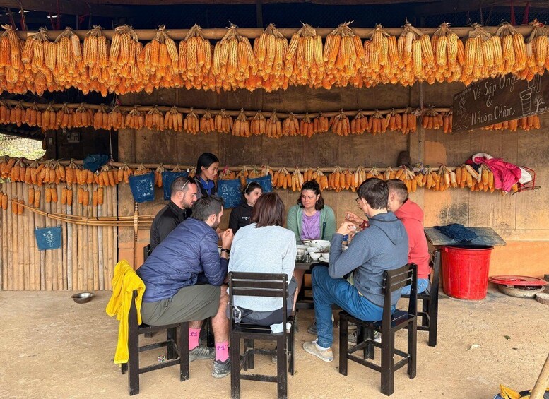 A group of people dining at an outdoor stall with corn hanging above. 5