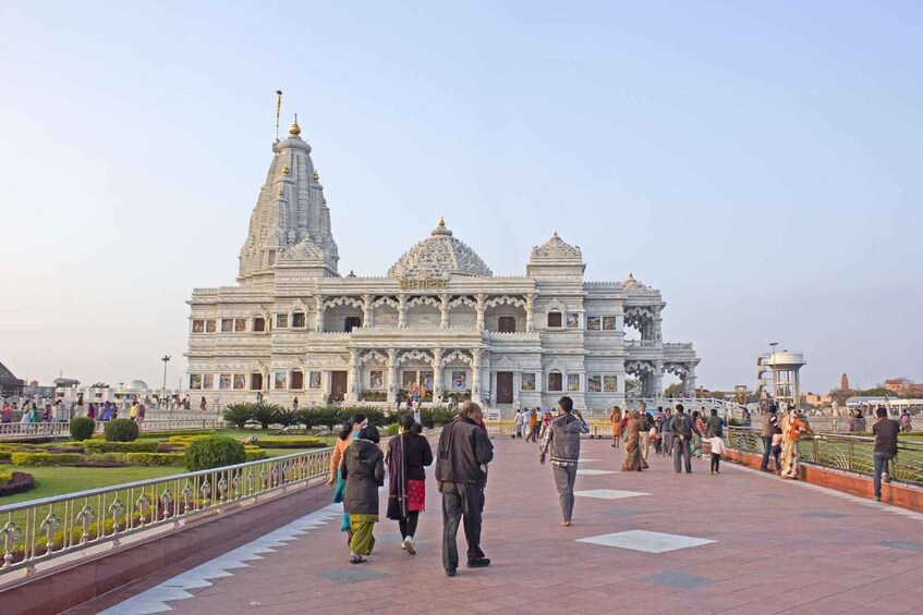A large white temple with multiple domes and a tall spire, surrounded by a paved walkway with people walking. 2