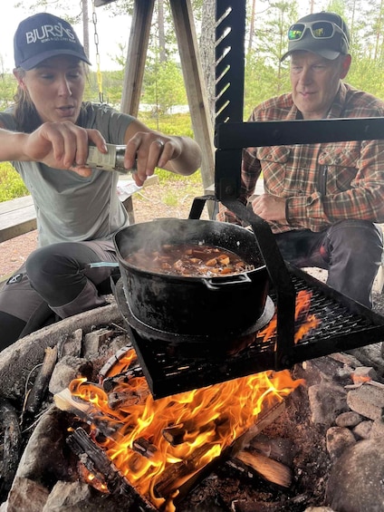 Two people cooking outdoors with a portable stove over a fire. 4
