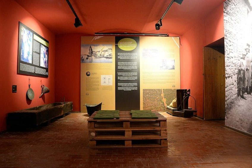 An indoor exhibit with informational displays, a wooden table, and a stone wall. 2