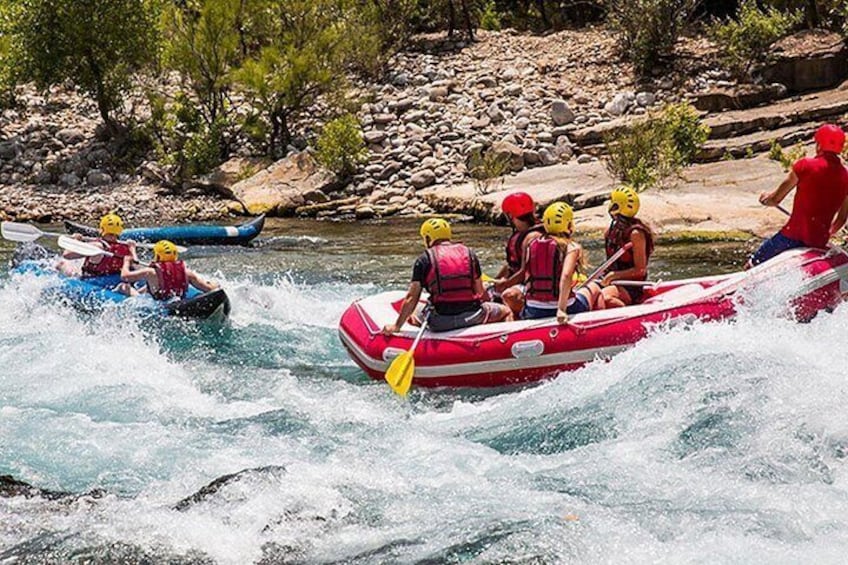 Menschen treiben auf Rafts auf einem Fluss, umgeben von felsigem Gelände und vereinzelter Vegetation. 5