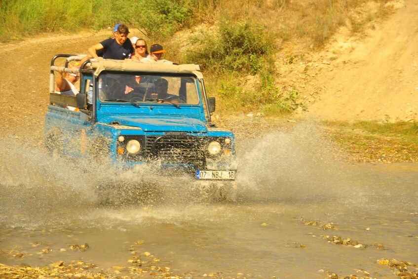 A blue off-road vehicle driving through a shallow water crossing, splashing water around. 3