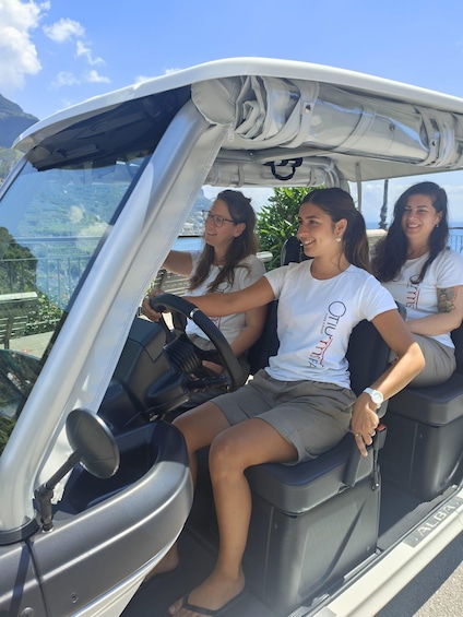 Three people in a golf cart with a scenic view of a coastal landscape. 1