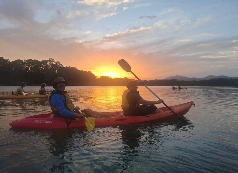 Two people kayaking on a calm lake during sunset. 1