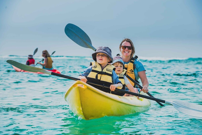A family in a yellow kayak on calm waters, with a clear sky and other kayakers in the background. 4
