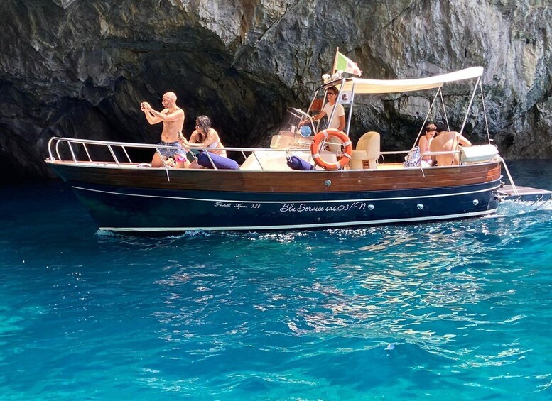 A boat named 'Blu Service' with passengers and a rocky cliff in the background. 1
