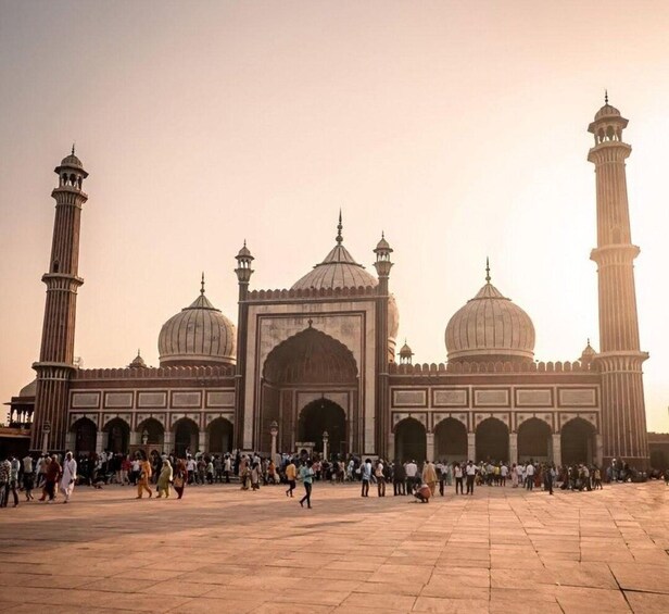 A large mosque with multiple domes and minarets, surrounded by a spacious courtyard with people walking around. 3