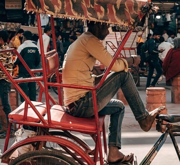 A man sitting on a red rickshaw in a busy street. 1