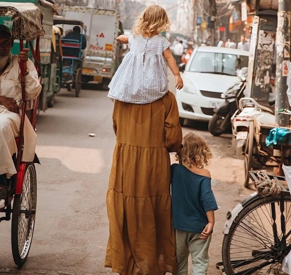 A person in a long brown dress with a child in a striped dress walking on a busy street with vehicles and bicycles. 5