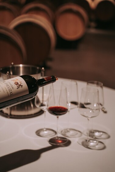 A bottle of Chateau de Fieuzal wine, a wine glass with red wine, and several empty wine glasses on a table. 1