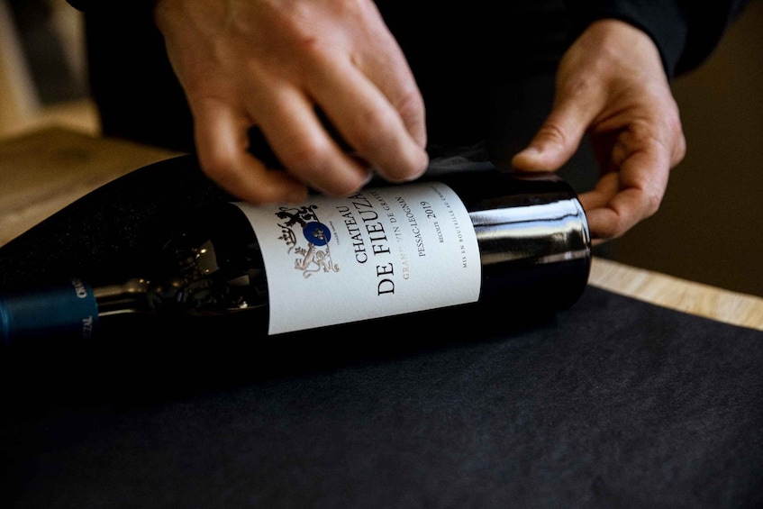 A person opening a bottle of wine with a label that reads 'DE CHATEAU DE FIEUEUZ.' 3