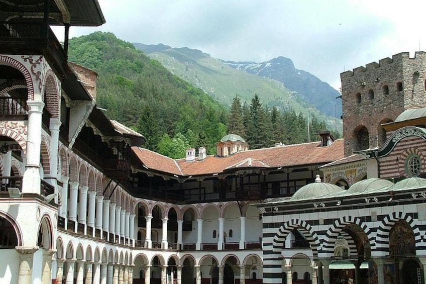 A historic building with arches, domes, and a mountainous backdrop. 1