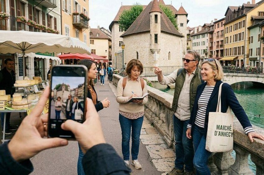 A group of people walking along a river in a historic town with buildings and a bridge in the background. 4