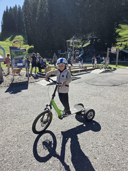 A child on a green electric skateboard in a park with a map sign and playground equipment in the background. 2