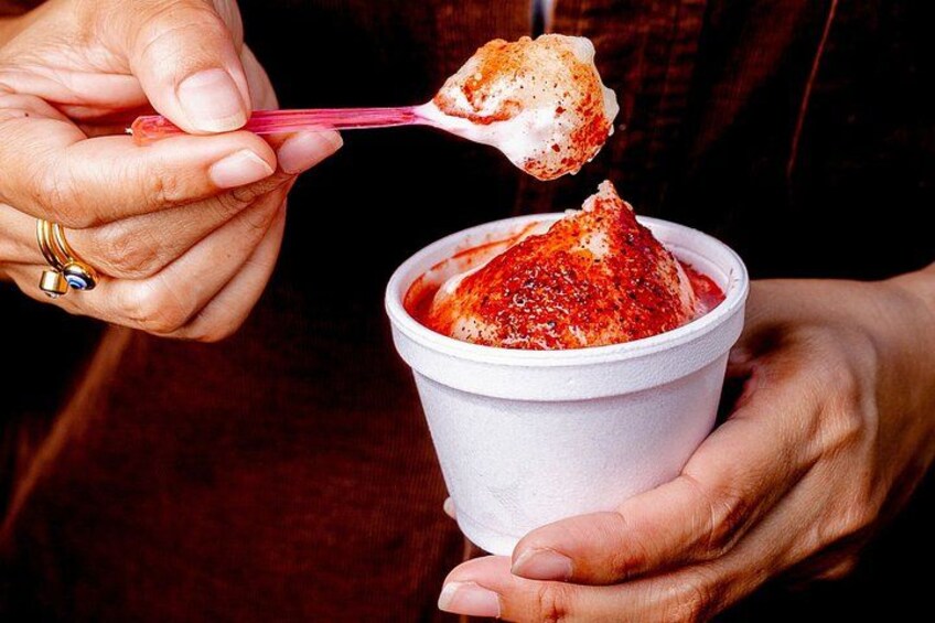 Una persona sosteniendo una taza con comida roja y usando una cuchara para levantar una porción. 2