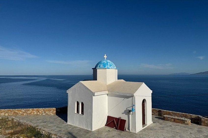 A white church with a blue dome and a cross on top, overlooking the sea. 2