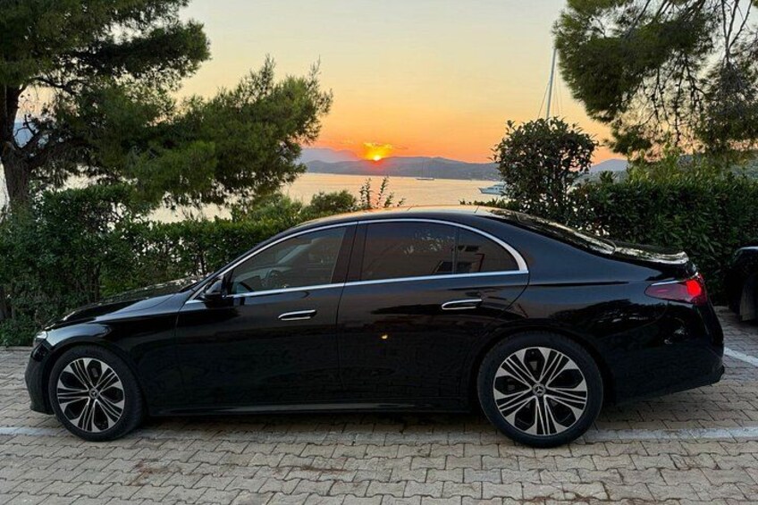 A black sedan parked on a paved surface with a sunset in the background. 4