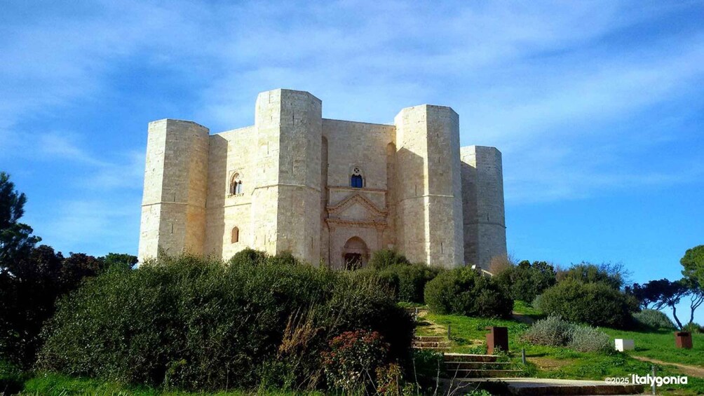 A historic castle with a central tower and two side towers, surrounded by greenery and a clear sky. 5