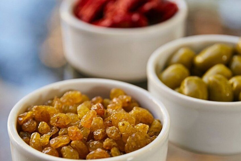 Trois bols de nourriture : un contenant des raisins secs, un contenant des olives et un contenant des fruits secs. 2