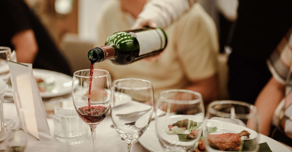 A person pouring red wine into a glass at a dining table with plates of food. 3