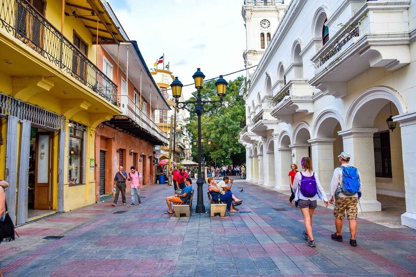A pedestrian street with buildings, a clock tower, and people walking and sitting. 2