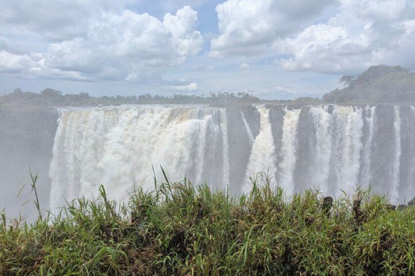 Een grote waterval met meerdere watertonnen, omgeven door groen en een bewolkte lucht. 3