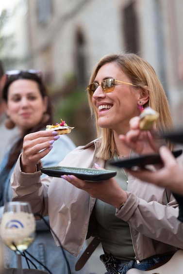 A person holding a plate with food, another person with a drink, and a blurred background suggesting an outdoor setting. 1
